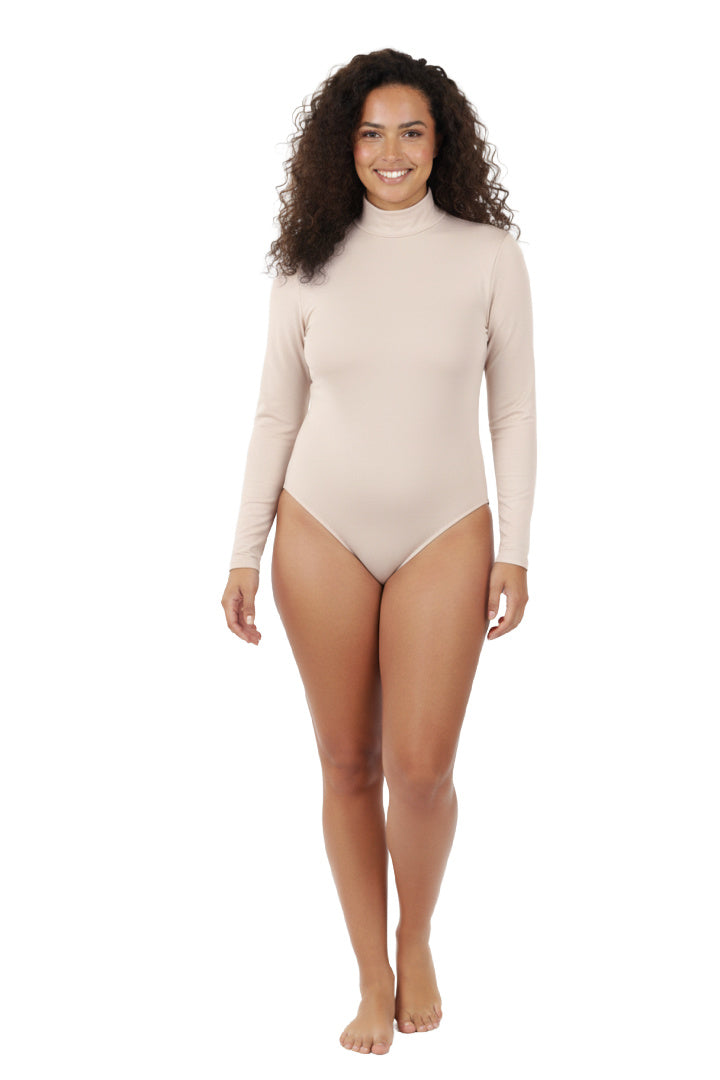 A full-length, studio shot of a smiling woman with curly hair wearing a simple, skin-tone or beige long-sleeve bodysuit with a mock neck. She is standing with her hands on her hips against a white background.