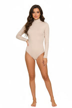 A full-length, studio shot of a smiling woman with wave hair wearing a simple, beige long-sleeve bodysuit with a mock neck. She is standing with her hand on her hip against a white background. 