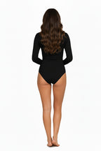 A full-length, studio shot of a smiling woman with wave hair wearing a simple, black long-sleeve bodysuit with a mock neck. She is standing with her hands on her hips against a white background. Back