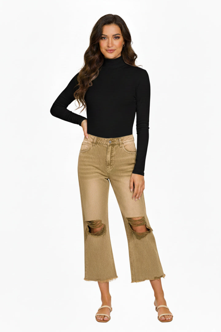A full-length, studio shot of a smiling woman with wave hair wearing a simple, black long-sleeve bodysuit with a mock neck with a jean. She is standing with her hand on her hip against a white background. 
