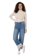 A model wearing a pair of light blue, high-rise, wide-leg jeans with a contrasting wide cuff at the ankle. The jeans have a classic five-pocket design and are paired with a beige top and white shoes. The model is standing in a studio setting.