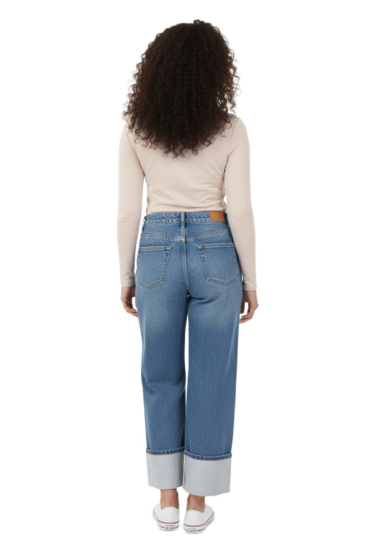 A model wearing a pair of light blue, high-rise, wide-leg jeans with a contrasting wide cuff at the ankle. The jeans have a classic five-pocket design and are paired with a beige top and white shoes. The model is standing in a studio setting. Back