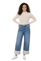 A model wearing a pair of light blue, high-rise, wide-leg jeans with a contrasting wide cuff at the ankle. The jeans have a classic five-pocket design and are paired with a beige top and white shoes. The model is standing in a studio setting. Front