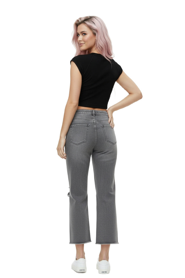 A model wearing a pair of ash-black, high-rise, wide-leg cropped jeans with distressed ripped knees and a frayed raw hem. The model is standing against a white background. Back