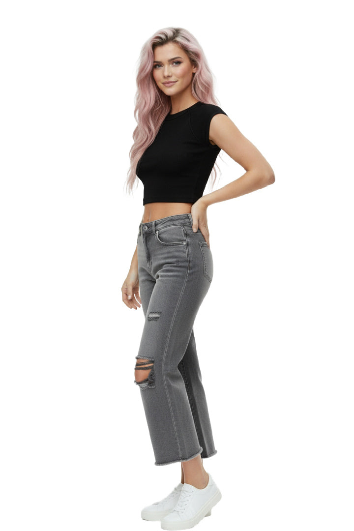 A model wearing a pair of ash-black, high-rise, wide-leg cropped jeans with distressed ripped knees and a frayed raw hem. The model is standing against a white background. Side