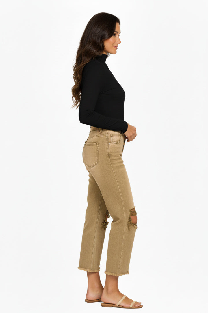 A model wearing a pair of camel, high-rise, wide-leg cropped jeans with distressed ripped knees and a frayed raw hem. The model is standing against a white background. Side