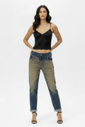Full-body shot of a female model wearing vintage oxyde distressed boyfriend jeans with a black satin camisole and black high-heeled sandals, standing against a white background.