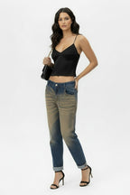 Full-body shot of a female model wearing vintage oxyde distressed boyfriend jeans with a black satin camisole and black high-heeled sandals, standing against a white background,one side.
