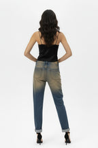 Back full-body shot of a female model wearing vintage oxyde distressed boyfriend jeans with a black satin camisole and black high-heeled sandals, standing against a white background.