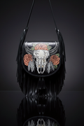 Black genuine leather shoulder bag with long fringe and a bold skull, feather, and rose design on the front flap, displayed against a dark background.